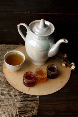 Ahşap tepsi üzerinde ev yapımı Berry üç küçük kavanoz reçel. Sağlıklı gıda fikirler. Çaydanlık ve yeşil çay bir arka plan üzerinde çay fincanı. Gül ahşap bir masa bir gümüş kaşık yanında bastırdı