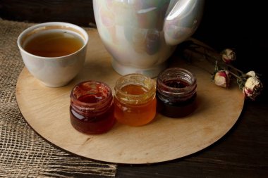 Porselen ile hizmet tabloyu kapatın. Çay bardağı, pot, gümüş kaşık, cam daire. Ahşap tepsi ile ahududu, çilek, yaban mersini üç küçük kavanoz reçel. Ev pişmiş yulaf ezmesi ve Hindistan cevizi bisküvi cockie