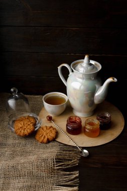 Ahşap tepsi üzerinde ev yapımı Berry üç küçük kavanoz reçel. Sağlıklı gıda fikirler. Çaydanlık ve yeşil çay bir arka plan üzerinde çay fincanı. Gül ahşap bir masa bir gümüş kaşık yanında bastırdı