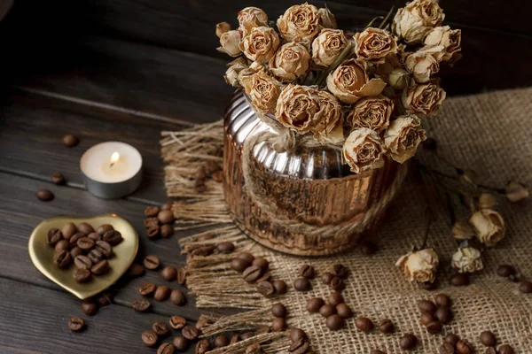 Bir masa örtüsü preslenmiş çiçek ile bronz cam vazo. Altın kalp şeklindeki uçan daire kavrulmuş kahve çekirdekleri ile. Saf arabica ahşap bir masa üzerinde. Mum arka planda. Aromatik Kahvaltı