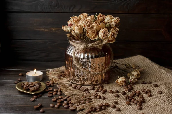 Bir masa örtüsü preslenmiş çiçek ile bronz cam vazo. Altın kalp şeklindeki uçan daire kavrulmuş kahve çekirdekleri ile. Saf arabica ahşap bir masa üzerinde. Mum arka planda. Aromatik Kahvaltı