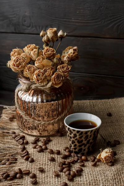 Bir masa örtüsü preslenmiş çiçek ile bronz cam vazo. Altın kalp şeklindeki uçan daire kavrulmuş kahve çekirdekleri ile. Saf arabica ahşap bir masa üzerinde. Mum arka planda. Aromatik Kahvaltı