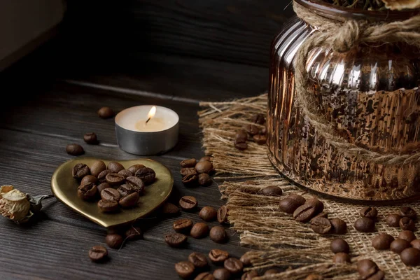 Bir masa örtüsü preslenmiş çiçek ile bronz cam vazo. Altın kalp şeklindeki uçan daire kavrulmuş kahve çekirdekleri ile. Saf arabica ahşap bir masa üzerinde. Mum arka planda. Aromatik Kahvaltı