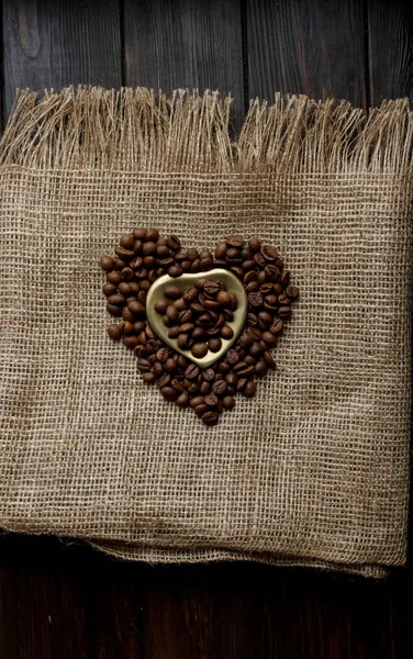 Flat lay of roasted coffee beans on a tablecloth with a golden heart shaped saucer and coffee mug. Cup of morning espresso and pressed roses. Romantic ideas