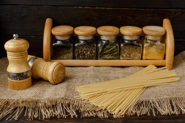 Ham yığın makarna keten masa örtüsü üzerinde dağınık. Sağlıklı yaşam ve beslenme alışkanlıkları. Gösterim amacıyla gıda blog. Cam baharat kavanozları - kümesi altı cam. Evde makarna pişirme. Tuz ve biber