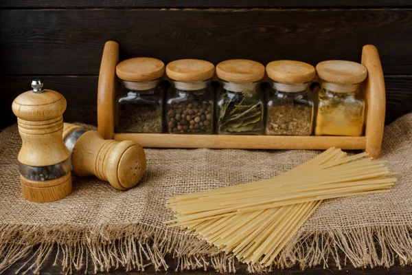 Ham yığın makarna keten masa örtüsü üzerinde dağınık. Sağlıklı yaşam ve beslenme alışkanlıkları. Gösterim amacıyla gıda blog. Cam baharat kavanozları - kümesi altı cam. Evde makarna pişirme. Tuz ve biber