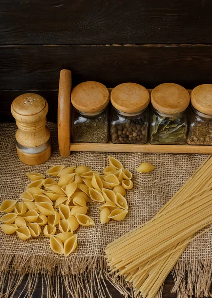 Ham yığın makarna keten masa örtüsü üzerinde dağınık. Sağlıklı yaşam ve beslenme alışkanlıkları. Gösterim amacıyla gıda blog. Cam baharat kavanozları - kümesi altı cam. Evde makarna pişirme. Tuz ve biber