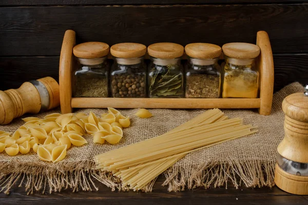 Ham yığın makarna keten masa örtüsü üzerinde dağınık. Sağlıklı yaşam ve beslenme alışkanlıkları. Gösterim amacıyla gıda blog. Cam baharat kavanozları - kümesi altı cam. Evde makarna pişirme. Tuz ve biber