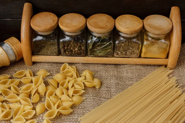 Ham yığın makarna keten masa örtüsü üzerinde dağınık. Sağlıklı yaşam ve beslenme alışkanlıkları. Gösterim amacıyla gıda blog. Cam baharat kavanozları - kümesi altı cam. Evde makarna pişirme. Tuz ve biber