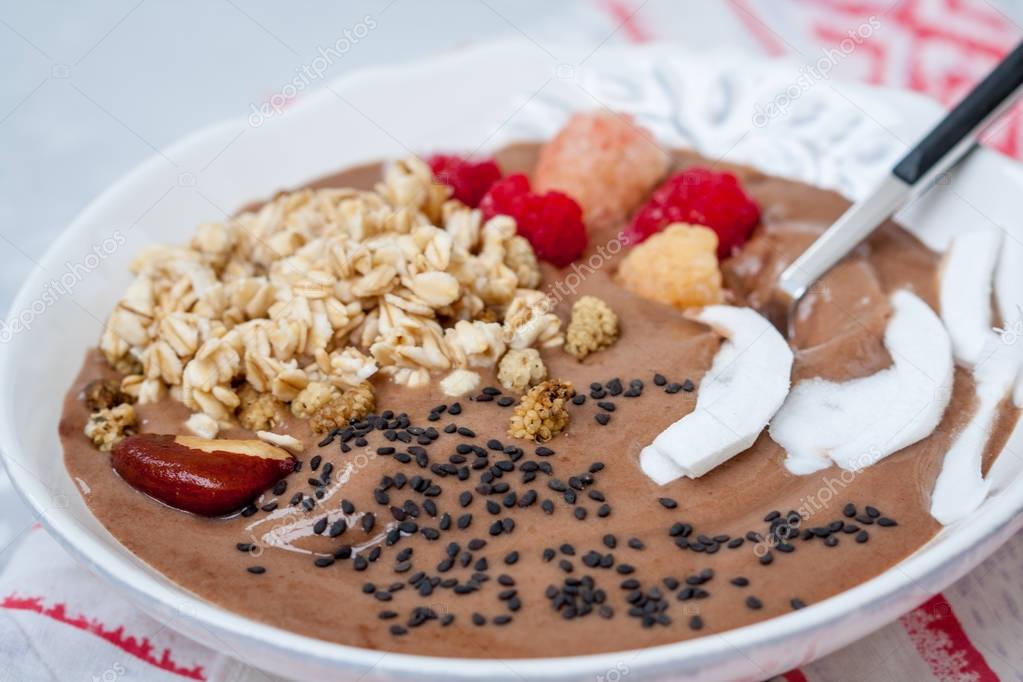 Chocolate smoothie bowl of oatmeal, sesame seeds and raspberries for breakfast