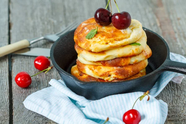 Homemade cottage cheese pancakes with cherries in a cast-iron frying pan.