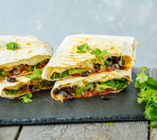 Burritos vegetarianos envueltos con frijoles, aguacate y queso en pizarra —  Fotos de Stock