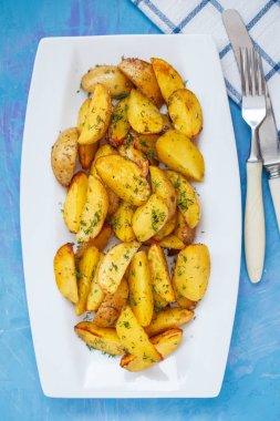 Fırında patates dilimleri ile beyaz bir tabak içinde otlar