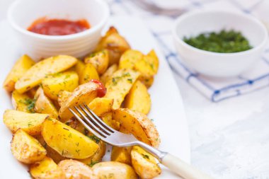 Fırında patates dilimleri ile beyaz bir tabak içinde otlar