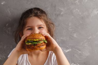 Küçük kız sağlıklı bir pişmiş tatlı patates hamburger yiyor wi