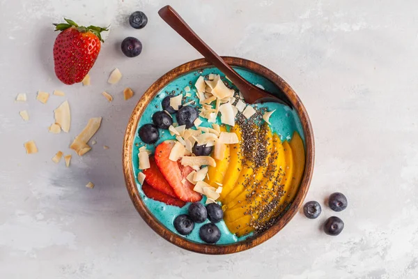 Berry blue smoothie bowl with mango and coconut, top view, copy