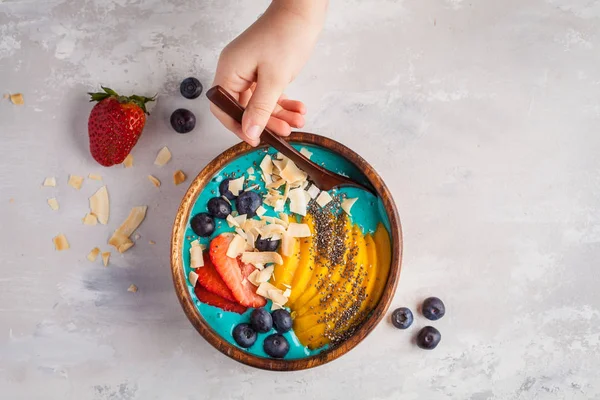 Berry blue smoothie bowl with mango and coconut, top view, copy