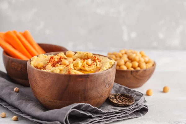 Hummus, fresh carrot sticks and boiled chickpeas in wooden bowls