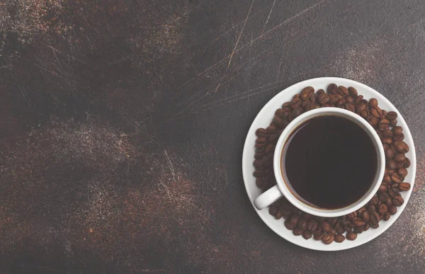 Kahve çekirdekleri ve karanlık paslı arka plan üzerinde beyaz bir fincan kahve.