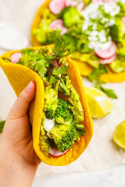 Tacos veganos de cúrcuma con rábano, brócoli y guacamole en la mano —  Fotos de Stock