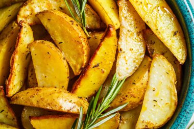 Baked potato wedges with rosemary in blue dish, top view. 