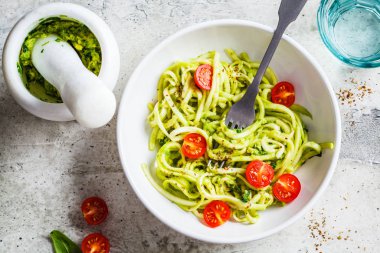 Pesto soslu kabak makarnası, avokado ve beyaz tabakta domates.