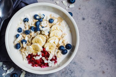 Bircher Müsli, böğürtlen, muz, reçel ve hindistan cevizi beyaz bir kasede, gri arka planda..
