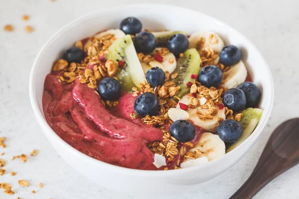 Pink berry smoothie bowl with fruits, berries and granola in white bowl on a white background. Healthy vegan food concept.