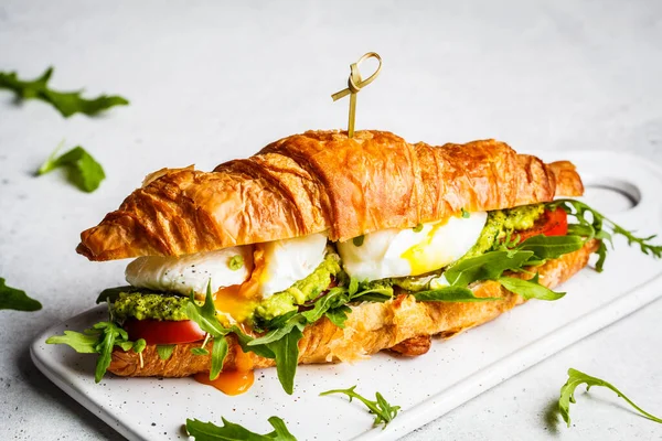 Beyaz tahtada haşlanmış yumurta, domates ve guacamole soslu kruvasan sandviçi. Kahvaltı konsepti..