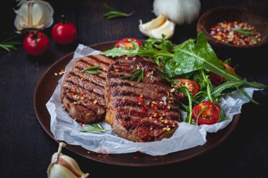 Ahşap tabakta roka ve domates salatası ile ızgara biftek, koyu arka plan..