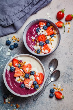 İki renkli meyve suyu kasesi, granola, yabanmersini ve hindistan cevizi, gri arka plan. Sağlıklı vejetaryen gıda kavramı.