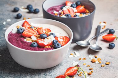 İki renkli meyve suyu kasesi, granola, yabanmersini ve hindistan cevizi, gri arka plan. Sağlıklı vejetaryen gıda kavramı.