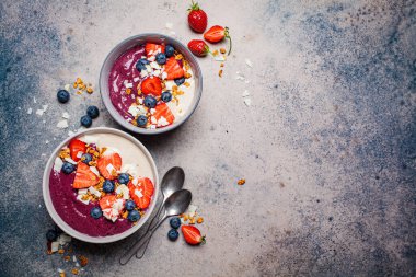 İki renkli meyve suyu kasesi, granola, yabanmersini ve hindistan cevizi, gri arka plan. Sağlıklı vejetaryen gıda kavramı.