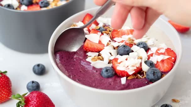 Mangiare con cucchiaio bacca frullato ciotola con muesli, fragole, mirtilli e cocco . — Video Stock