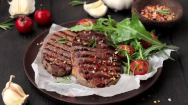 Ahşap tabakta roka ve domates salatası ile ızgara biftek, baharat serpiştirilmiş, koyu arkaplan.