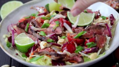Sebzeli Tayland salatası ve fındıklı beyaz kâse, koyu arkaplan üzerine limon suyu dök.. 