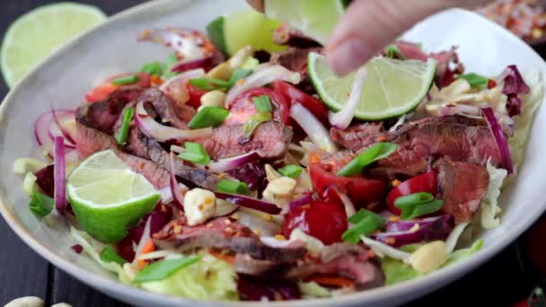 Thai marhahús saláta zöldségekkel és diófélékkel fehér tálban, citromlével, sötét alapon. — Stock videók