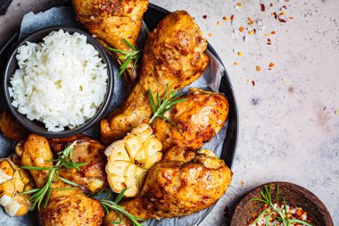 Kızarmış tavuk budu, pilav, sarımsak ve siyah bir tabakta otlar..