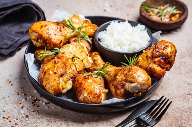 Kızarmış tavuk budu, pilav, sarımsak ve siyah bir tabakta otlar..