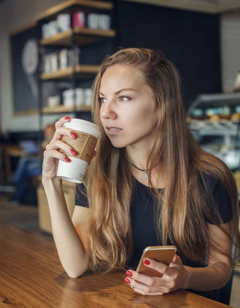 Woman with a cellphone drinking coffee and thinking