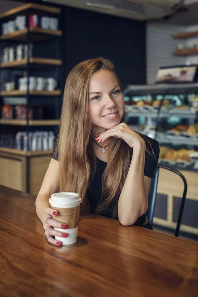 Mujer sentada a la mesa con un café sonriente —  Fotos de Stock