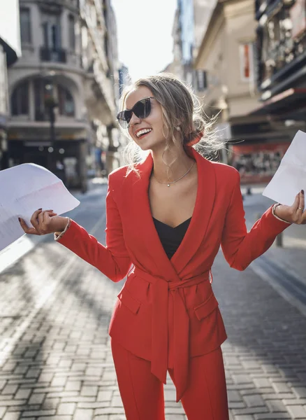 Модная женщина в красном костюме смеется, держа бумаги. — стоковое фото