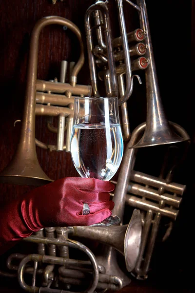 pipes of wind instruments on a wooden background in the center of a gloved hand with a ring holding a glass with a drink.