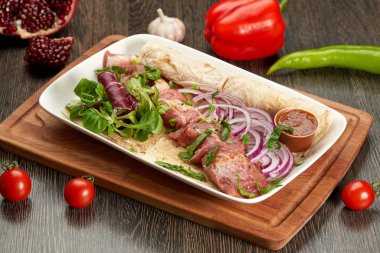 Beyaz tabakta barbekü ve soslu ve soğanlı ahşap bir kesim tahtası.