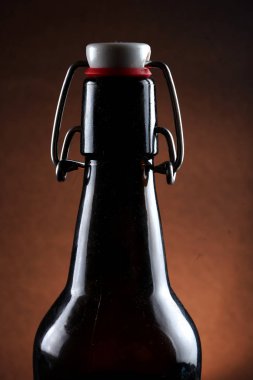 Siyah arka planda kapağı koyu camlı bira şişesi.