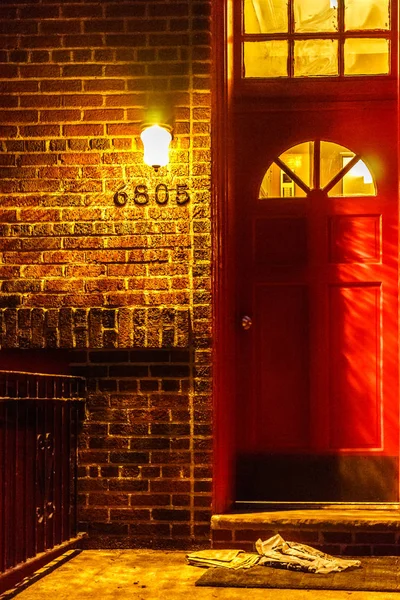 Porta rossa sul muro di mattoni, lato di una casa di notte con lampada a sospensione e giornale — Foto Stock