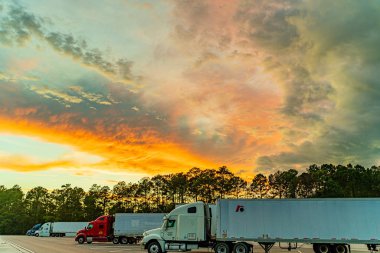 Georgia Usa 'daki ziyaretçi merkezi ve dinlenme alanı yaz günbatımının arka planına karşı gökyüzünde beyaz, turuncu, mavi ve koyu bulutlar ve ağır kamyonlar,