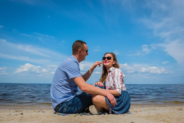 Egy szerető pár sittingon a strand közelében a víz játszik egymással, kék ég, a háttérben, süt a nap, széles látószögű, hosszú, fehér couds — Stock Fotó