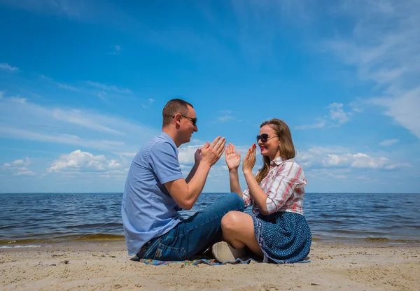 Egy szerető pár sittingon a strand közelében a víz játszik egymással, kék ég, a háttérben, süt a nap, széles látószögű, hosszú fehér felhők — Stock Fotó