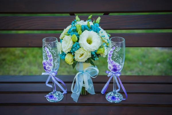 Wedding bouquet with stemware (a glass of champagne), in blue and violet colors, glasses decorated with flowers, standing on the bench, flat lay — Stock Photo, Image